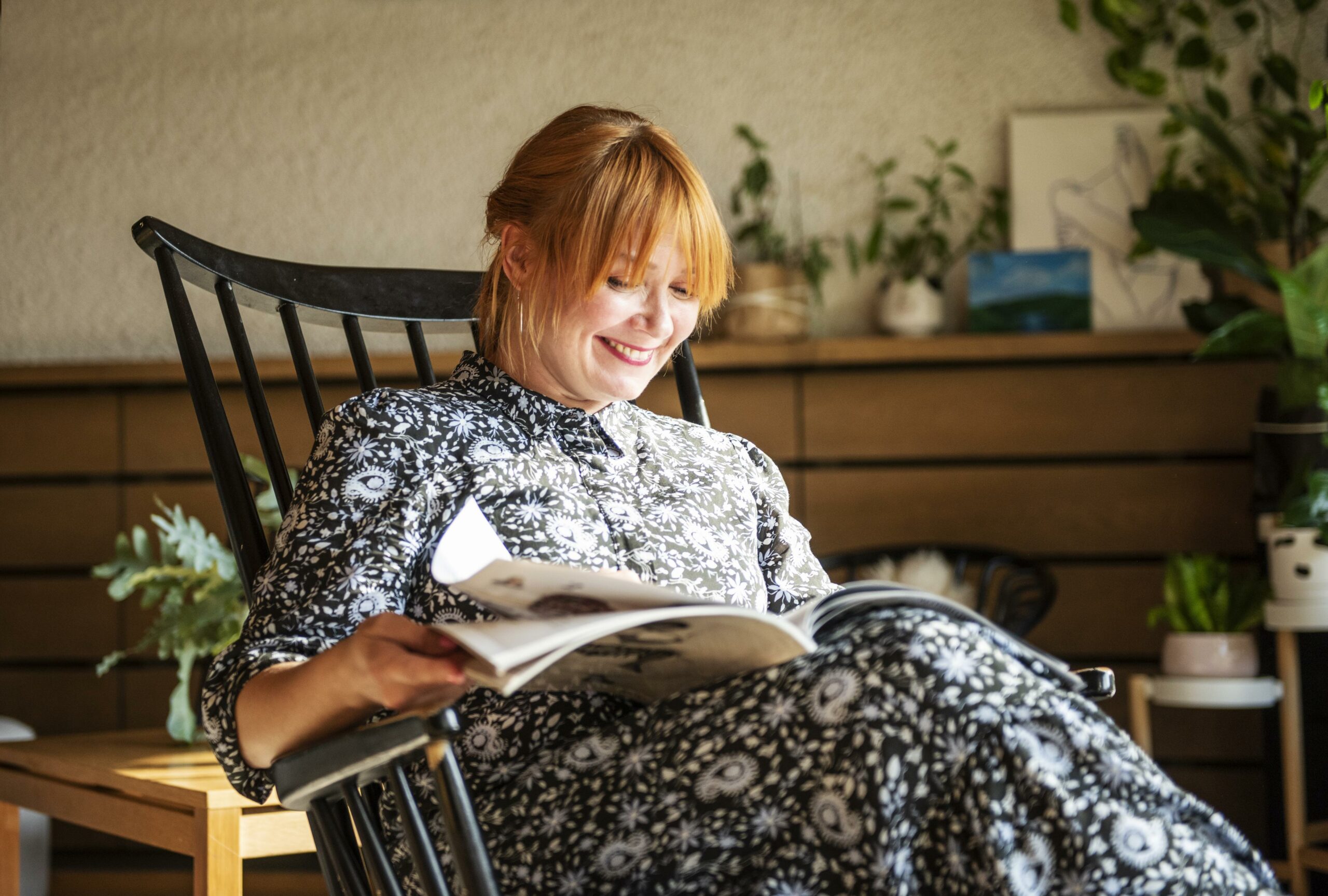 Muusikko Irina istuu kotonaan keinutuolissa ja lukee lehteä. 