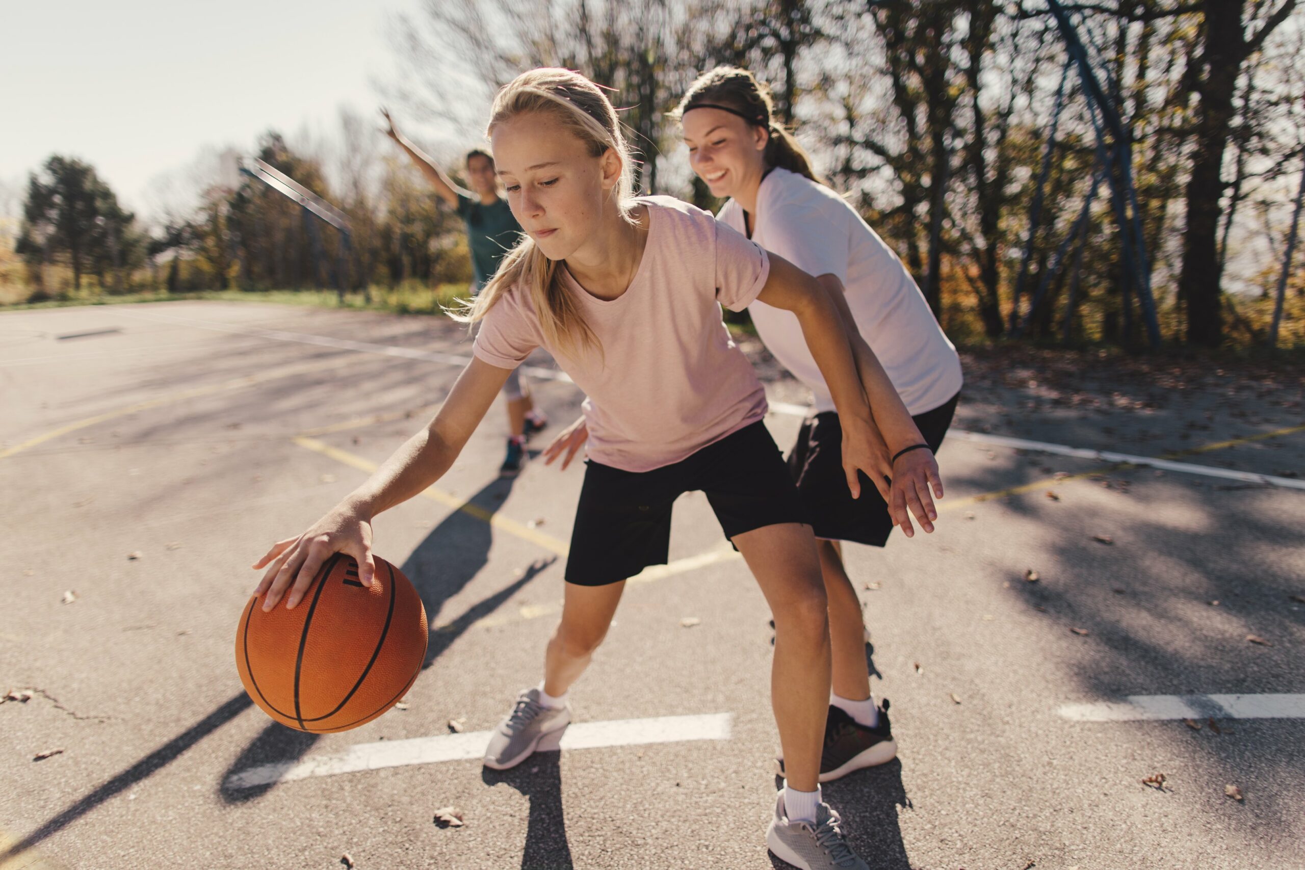 Tytöt pelaavat koripalloa ulkona.